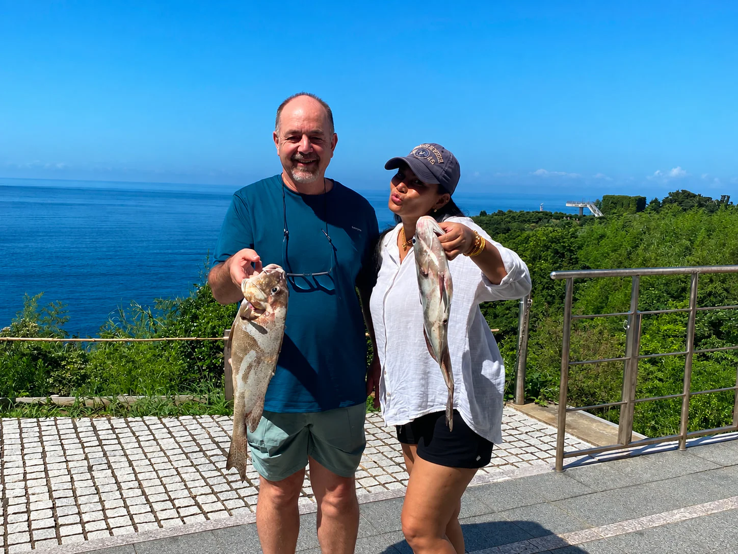 Two people by the sea, smiling with the fish they caught